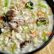 A close-up image of rice porridge with grouse meat, morel mushrooms, carrot, celery, and a scallion garnish