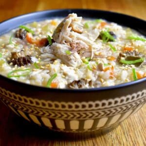 A bowl of rice porridge, garnished with celery, carrot, and scallions, served in a patterned blue bowl on a wooden surface