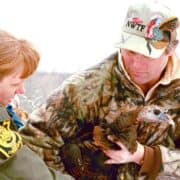 A National Wild Turkey Federation member holds a wild turkey next to a Pennsylvania Game Commission officer.