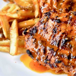 Turkey breast covered in a vibrant orange sauce, served with French fries on a white plate