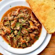 A dish of mushrooms in a brown broth served with a toasted slice of bread