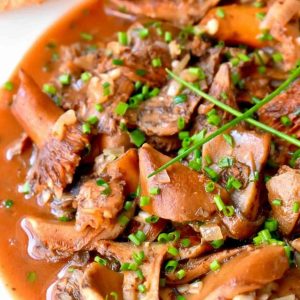 A close-up view of a dish of mushrooms in a brown broth topped with chives