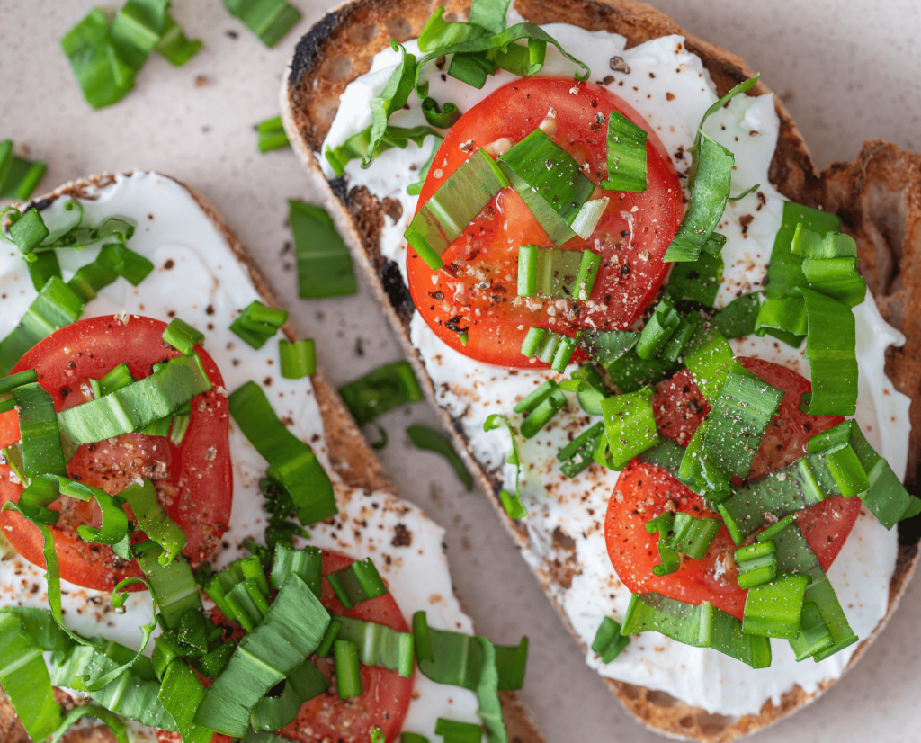 Toast with cream cheese, tomato slices, and wild garlic sprinkled on top.
