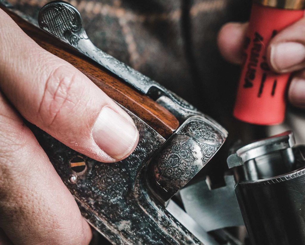 A quail hunter loading shotgun shells into his gun. 