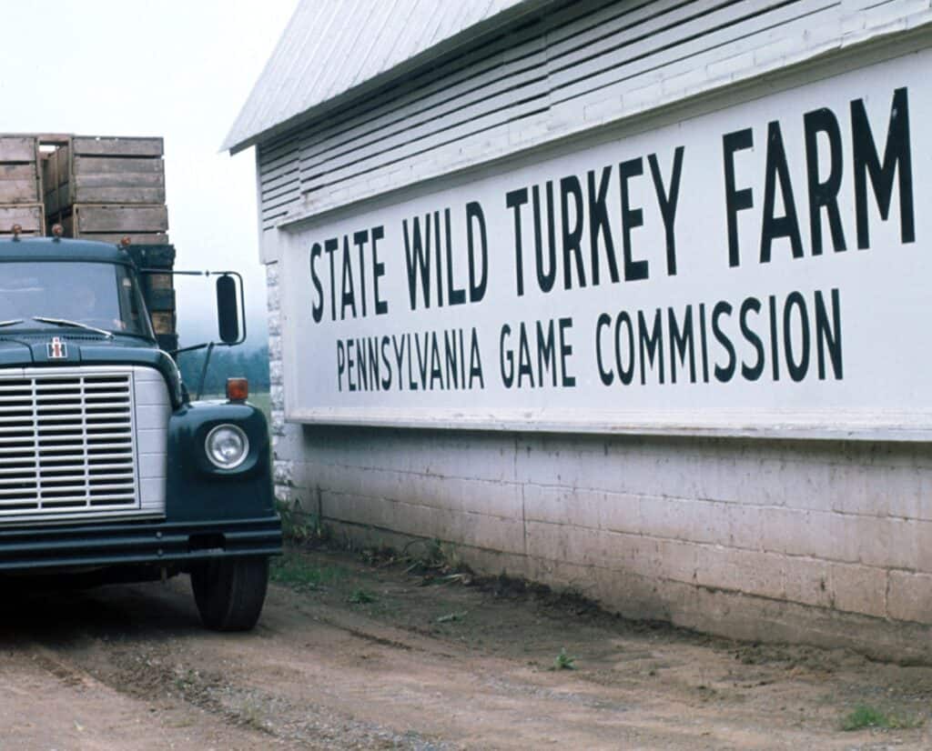 A green truck next to a large sign that states "State Wild Turkey Farm Pennsylvania Game Commission."