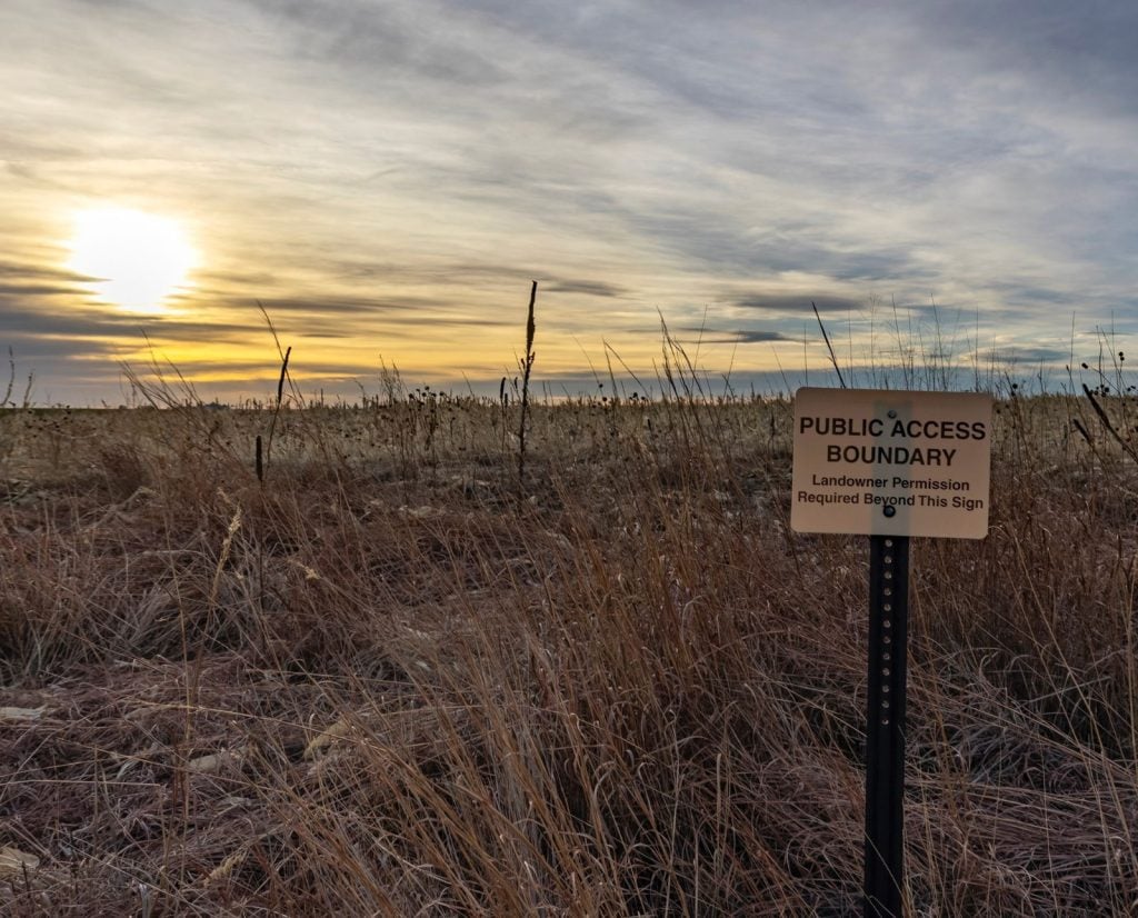 A sign marking the edge of a public hunting access boundary near a cornfield in Nebraska.