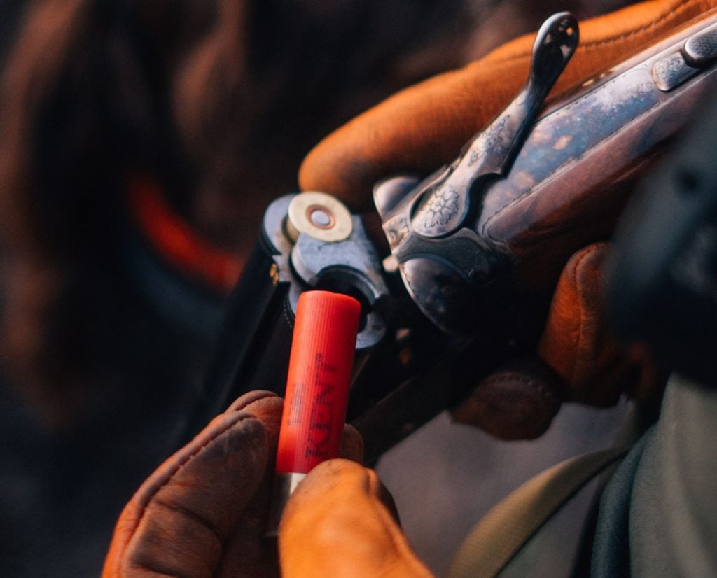 A man loads a shotgun cartridge into a side-by-side shotgun.