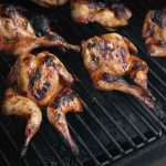 Spatchcocked quail coated in huli huli sauce, cooking on a grill
