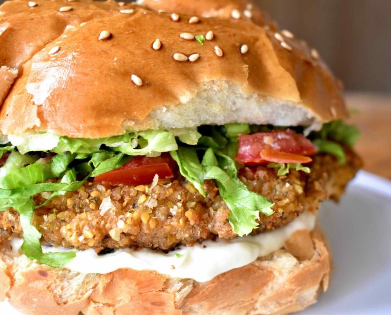 A crispy, fried patty topped with tomato and lettuce, served with white aioli sauce, on a hamburger bun