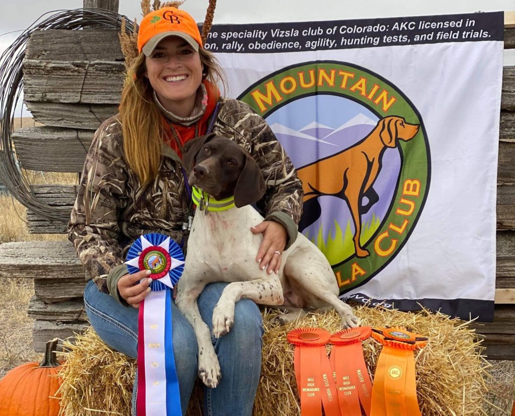 AKC Master Hunter test success with ribbons, a German Shorthaired Pointer pointing dog, and a professional dog handler.