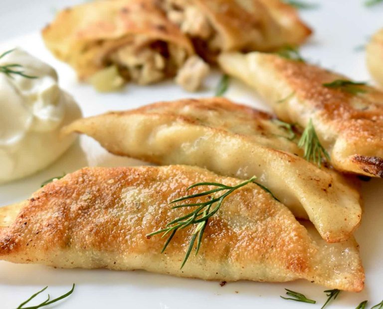 Pierogi dumplings filled with rabbit meat and chopped pickles fried to a golden brown and served on a white plate