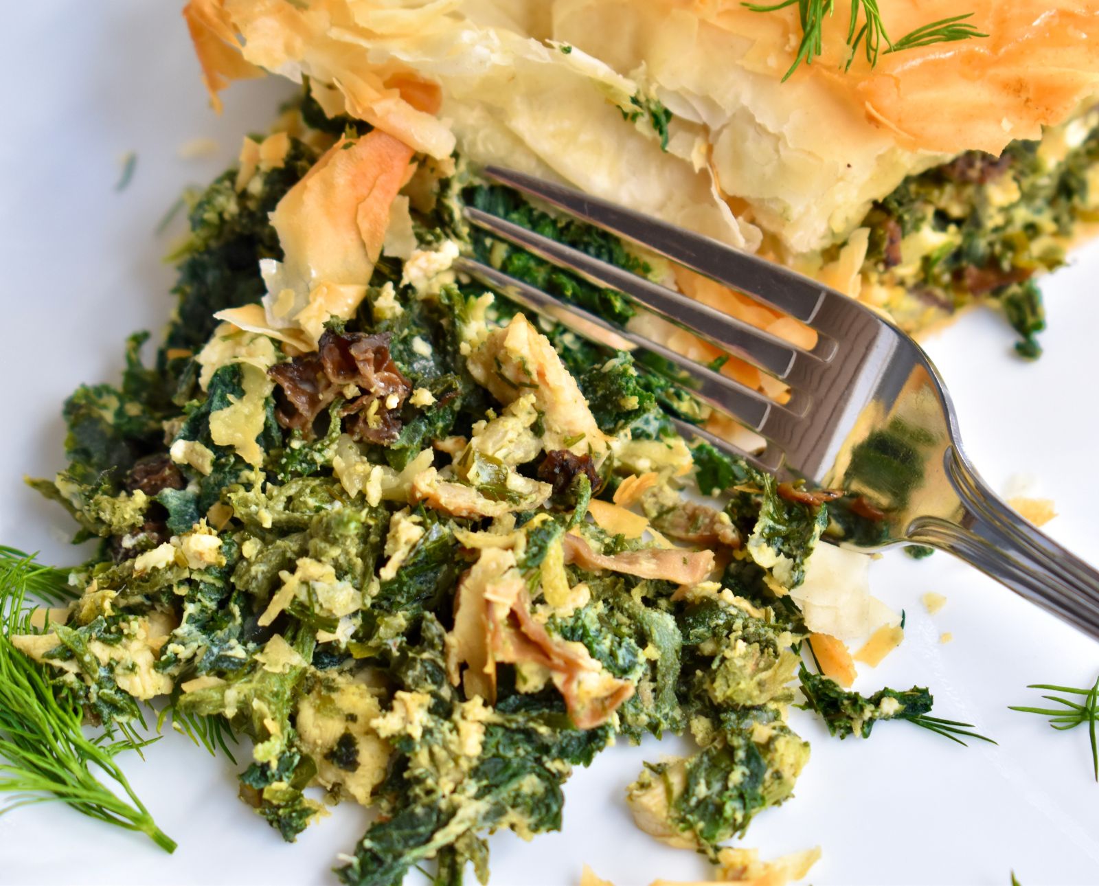 A fork slices into a ruffed grouse spanakopita pie with nettles and morel mushrooms.